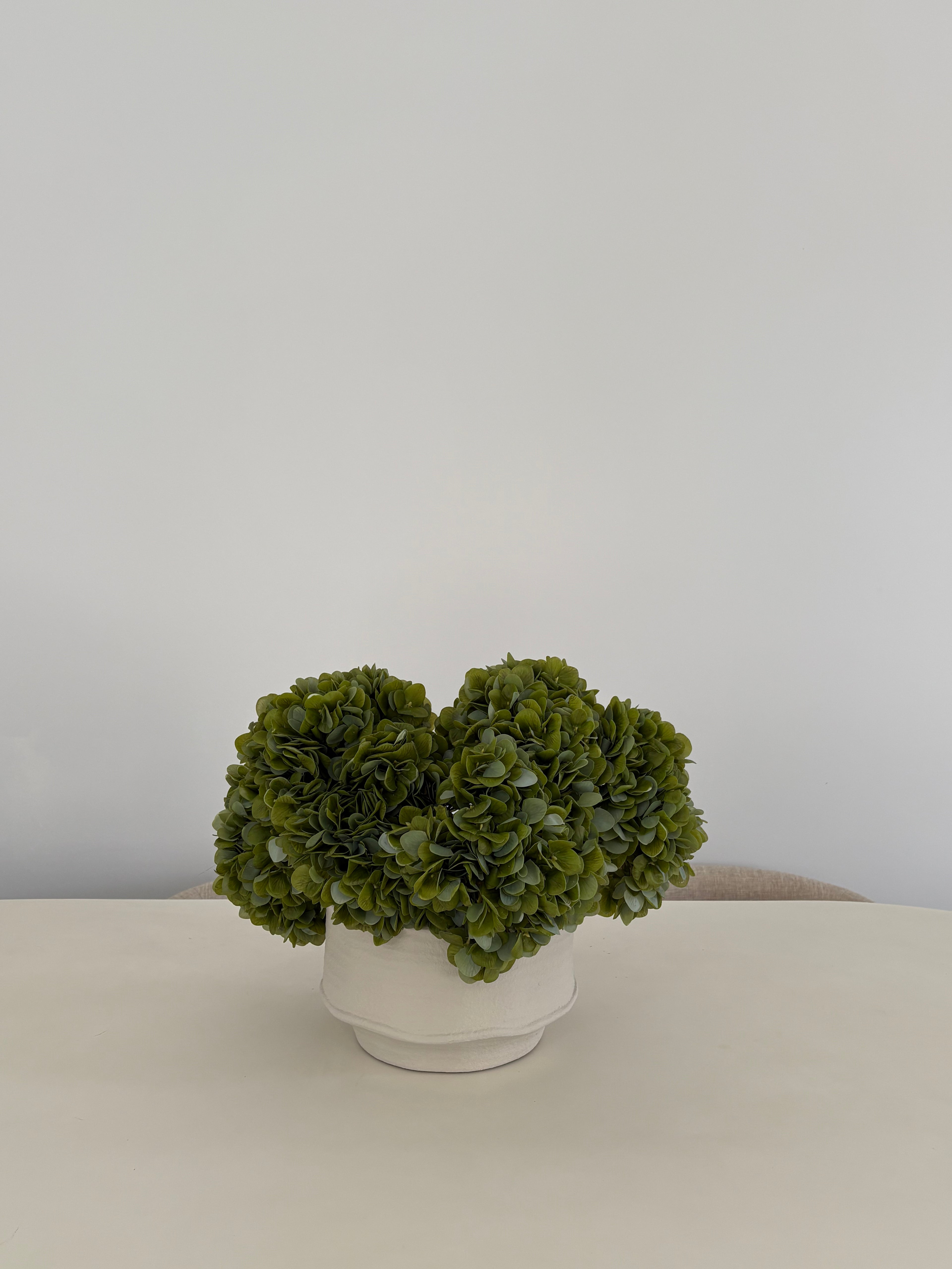 Artificial green hydrangea arrangement in textured white ceramic pot on table
