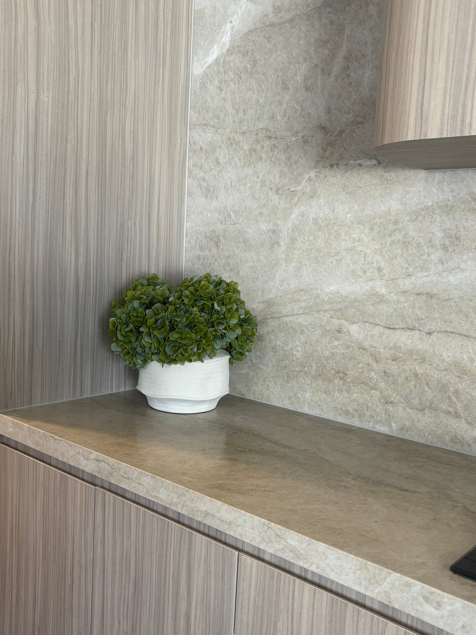 Real-touch green hydrangea arrangement in textured white pot placed in beige modern home interior