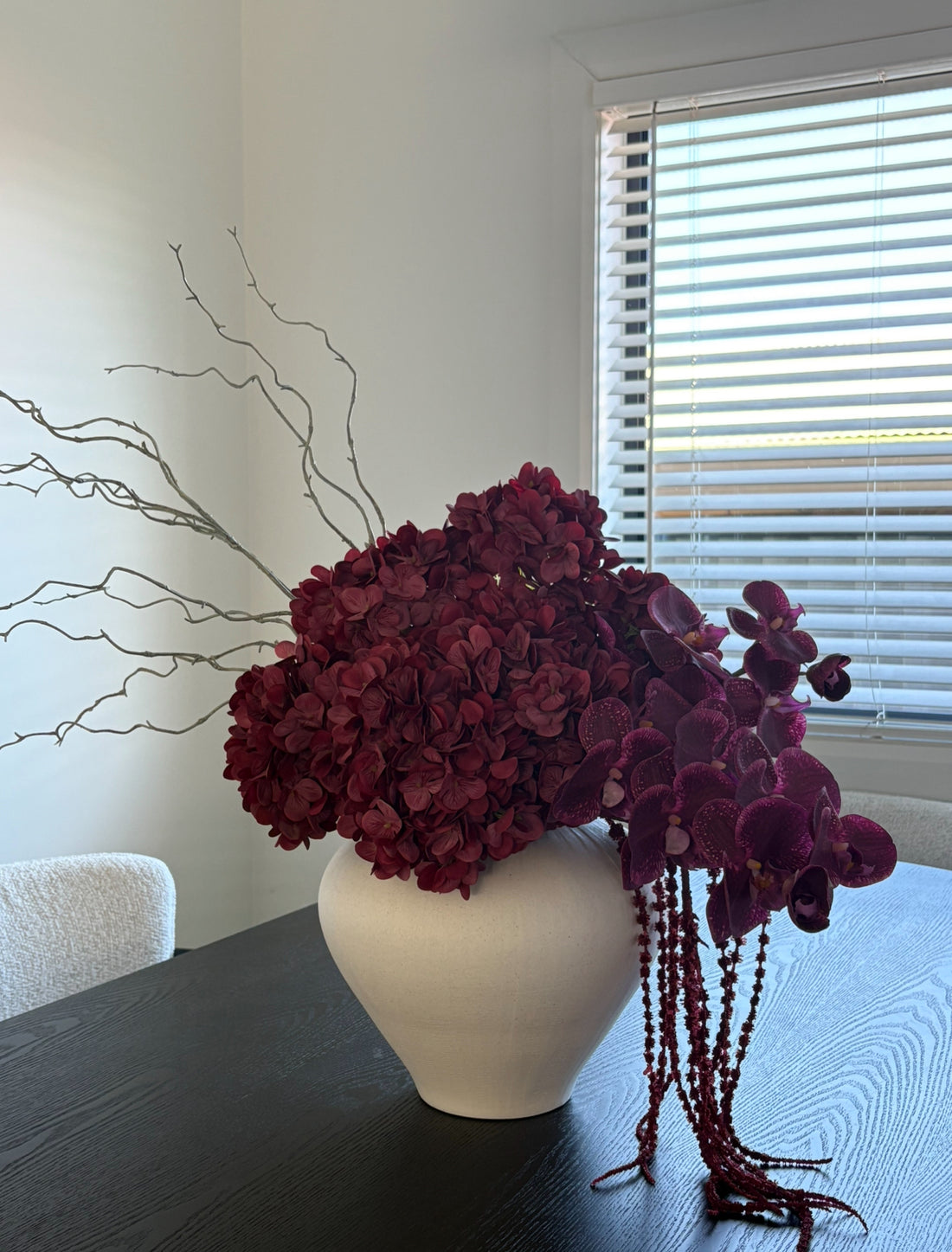 Burgundy artificial flower arrangement with real-touch orchids, hydrangeas, amaranthus, and twigs in a matte white vase.