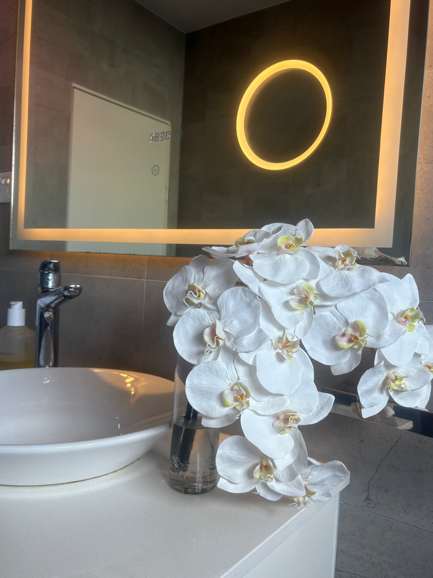Bathroom with a sink, mirror, and white orchids on a counter.