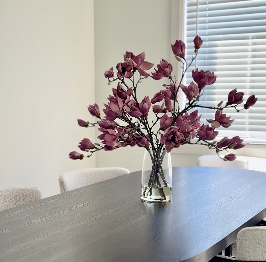 Plum magnolia arrangement in clear glass vase with faux water, real-touch artificial florals.