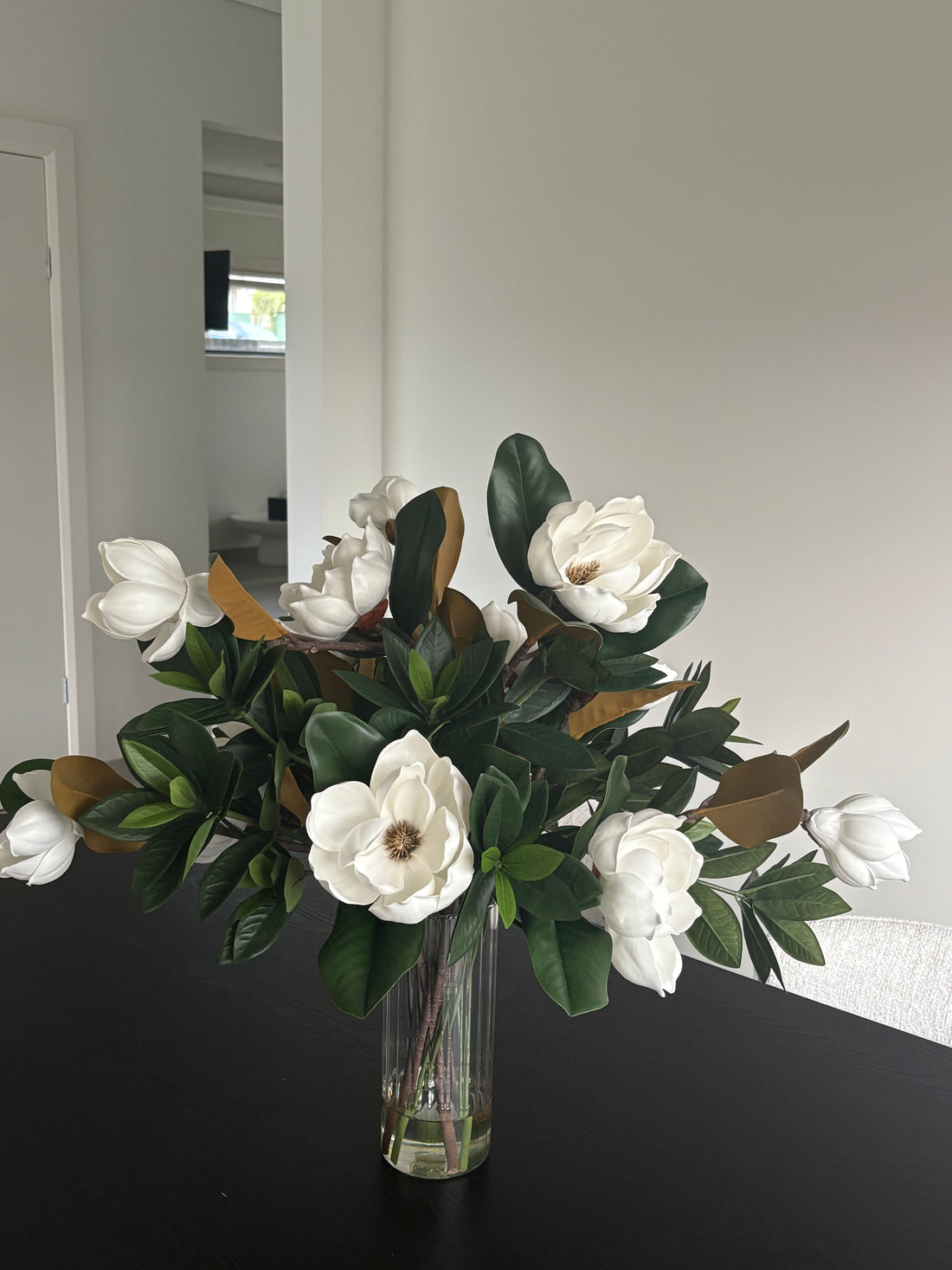 Large faux magnolia flowers arranged in clear glass vase