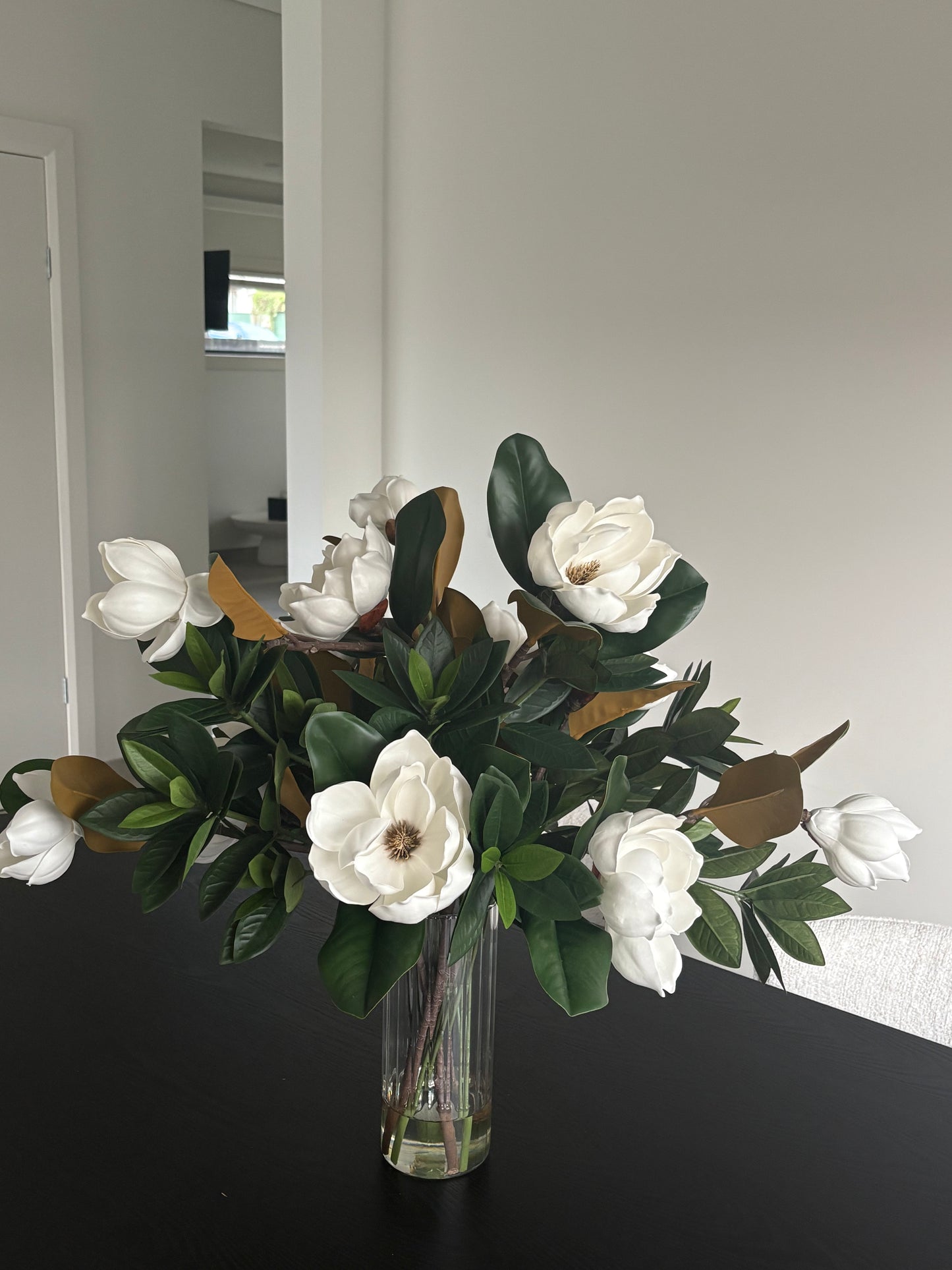 Large faux magnolia flowers arranged in clear glass vase