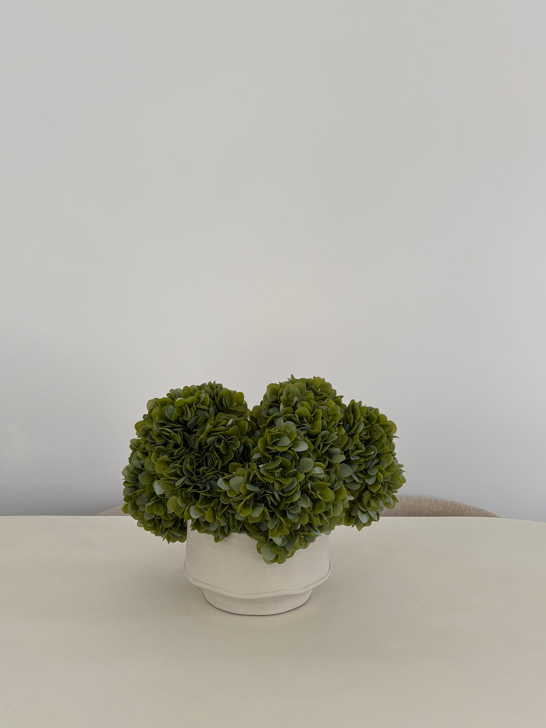 Artificial green hydrangea arrangement in textured white ceramic pot on table
