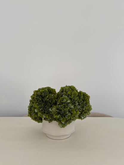 Artificial green hydrangea arrangement in textured white ceramic pot on table