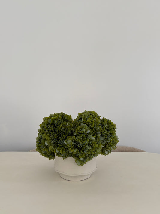 Artificial green hydrangea arrangement in textured white ceramic pot on table